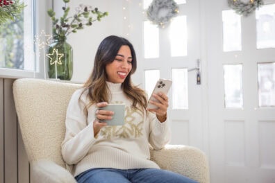 Young woman at home, sitting in an armchair and using her new smart phone.