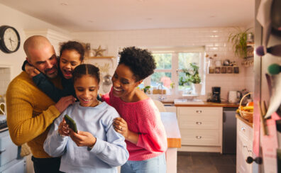 Family of four, smiling, looking at phone