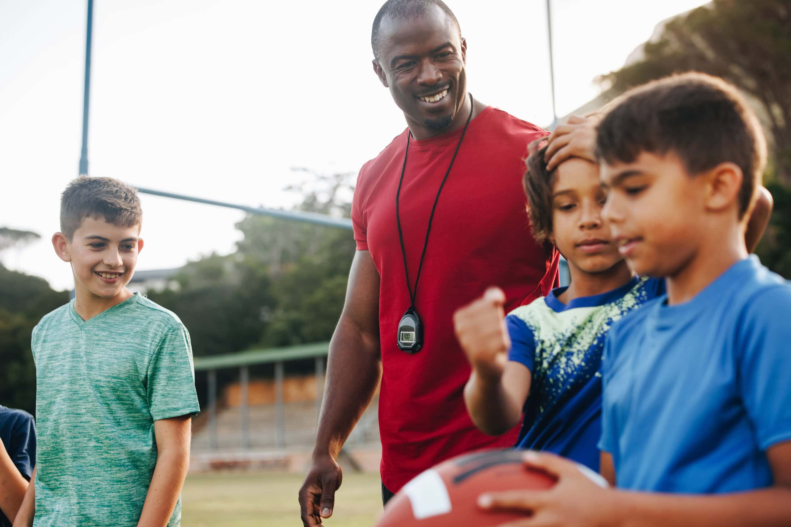 Coach training an elementary school football team. Sports instructor having a practice session with a group of children in primary school. Student mentorship and development.