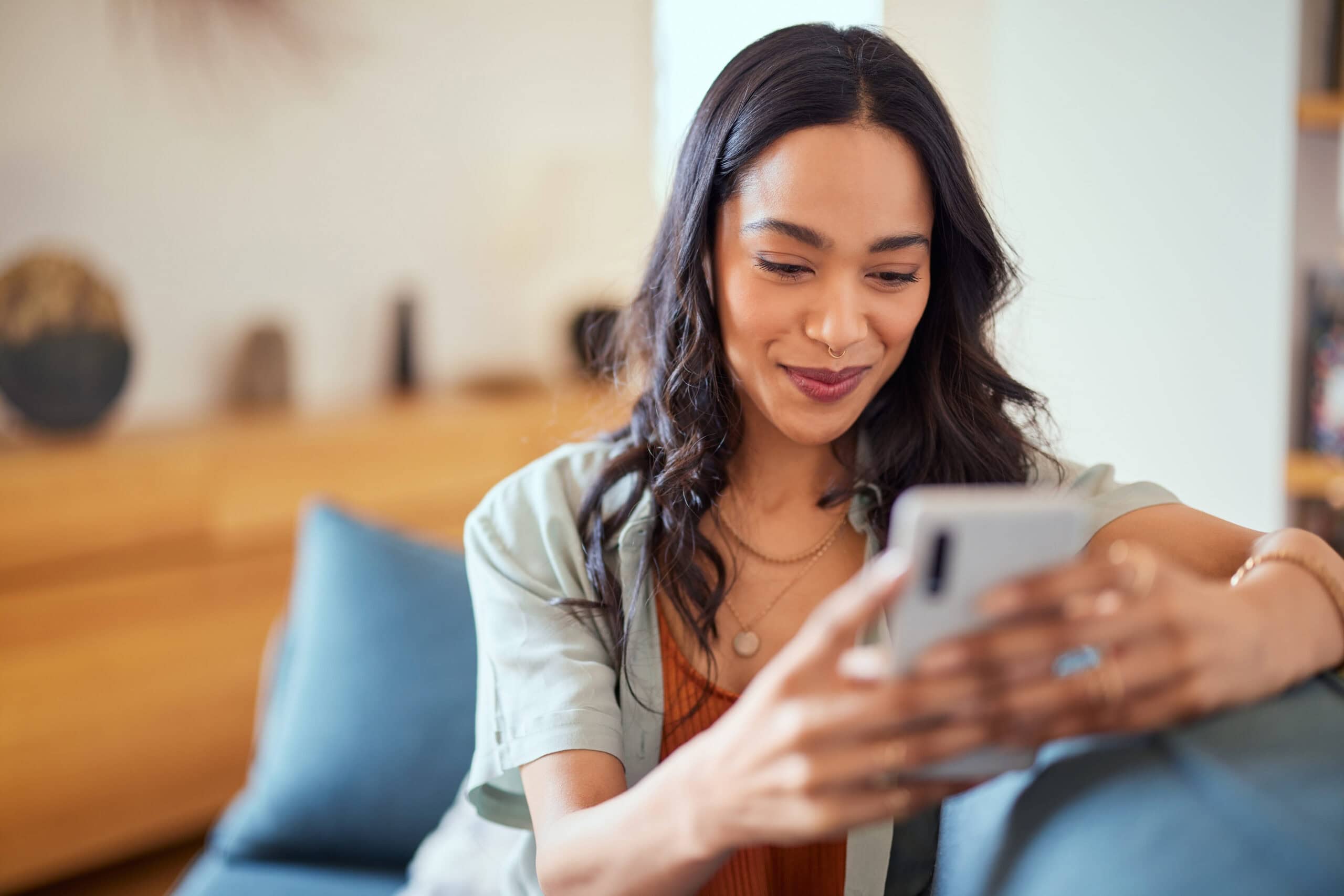 Happy, relaxed, beautiful woman using her smartphone while sitting on sofa at home.