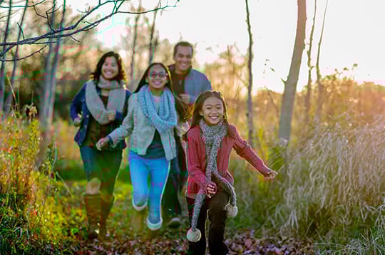 A family of four walking outside on a fall day, smiling and laughing.