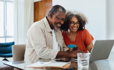 Happy, smiling older Black couple using a laptop while budgeting and paying bills together.