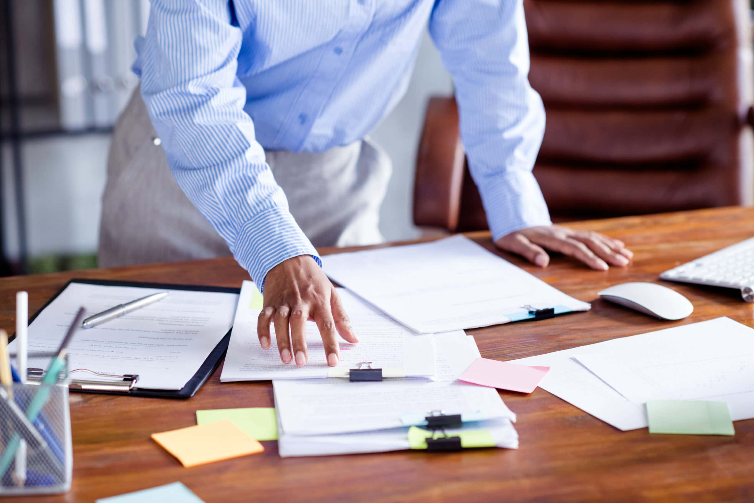 A young professional looks at her work desk that is covered in papers.
