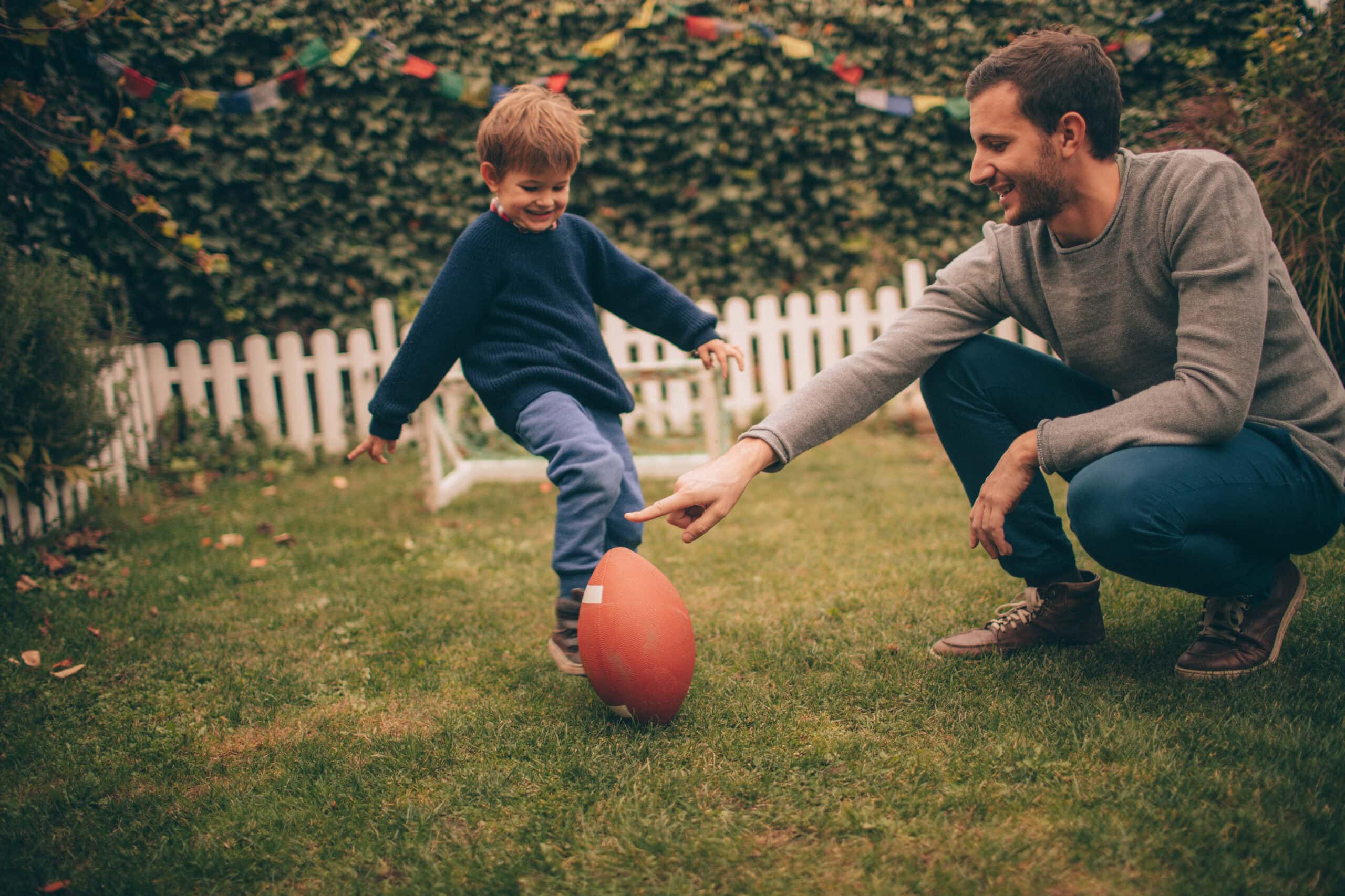 Photo of little smiling boy and his dad, playing American football in their backyard