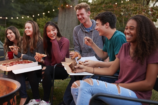 Teenagers at a fire pit eating pizza