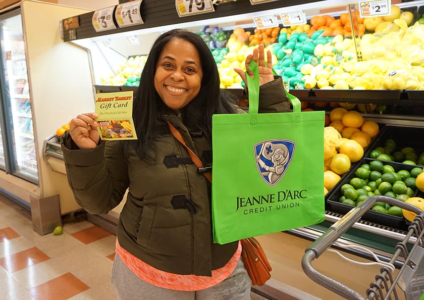 A woman in a grocery story holding a Jeanne D'Arc Credit Union bag